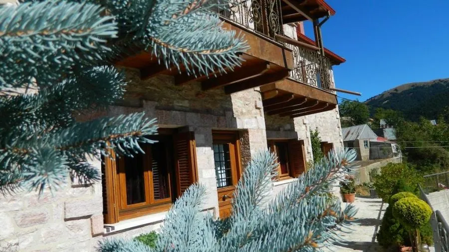 Το πέτρινο κτίριο με ξύλινα μπαλκόνια πίσω από ένα γαλάζιο έλατο
